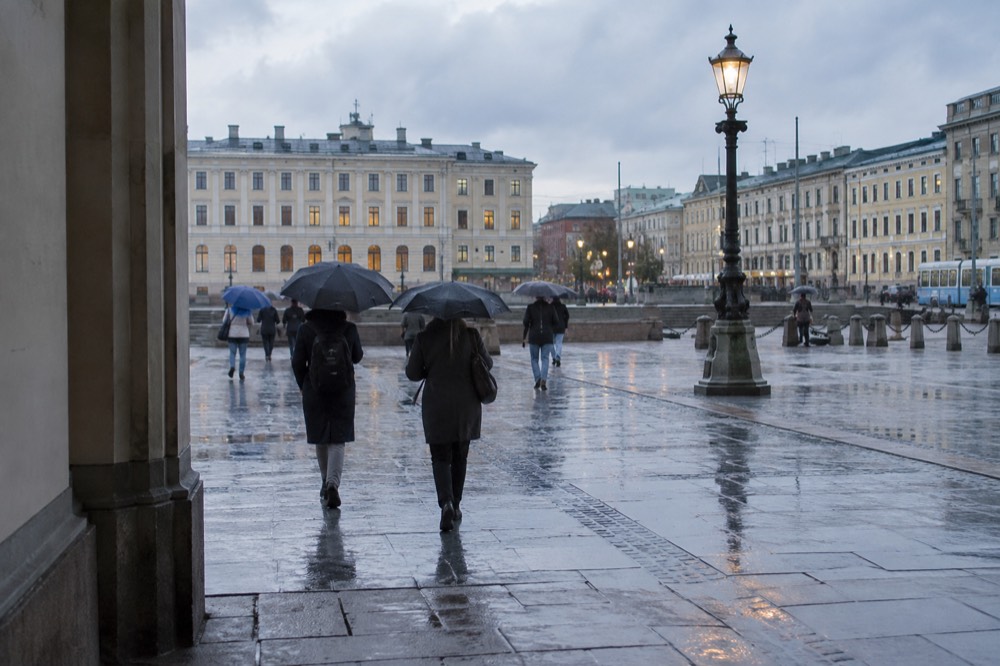 People with umbrellas walking past a lit cinema sign on a wet evening