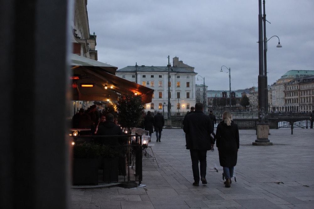 People outside lit bars on a narrow city street in the evening