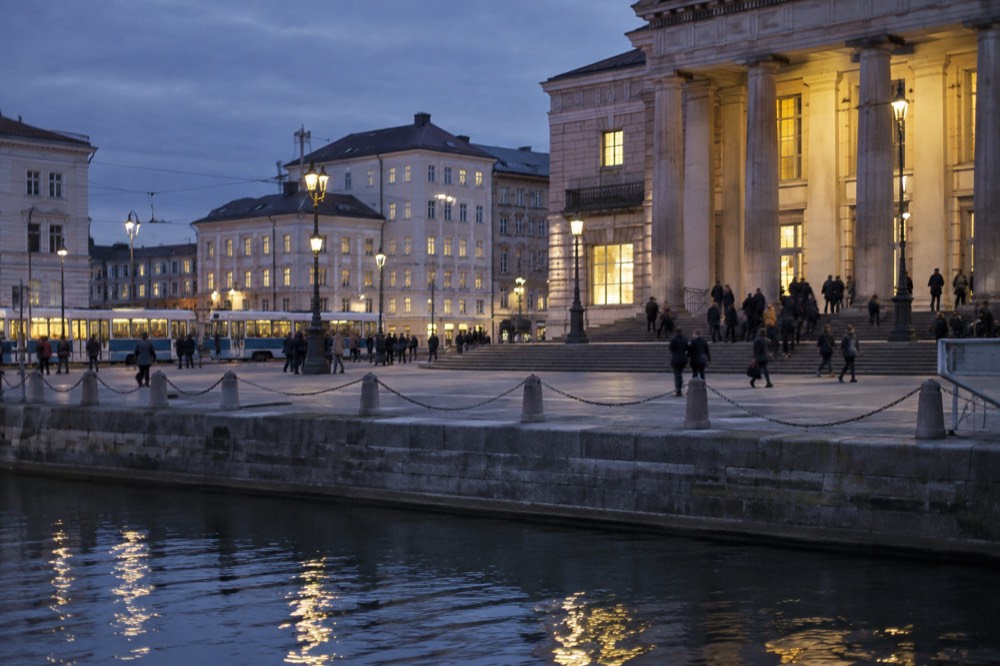 Museum building lit from inside with people on the steps at dusk