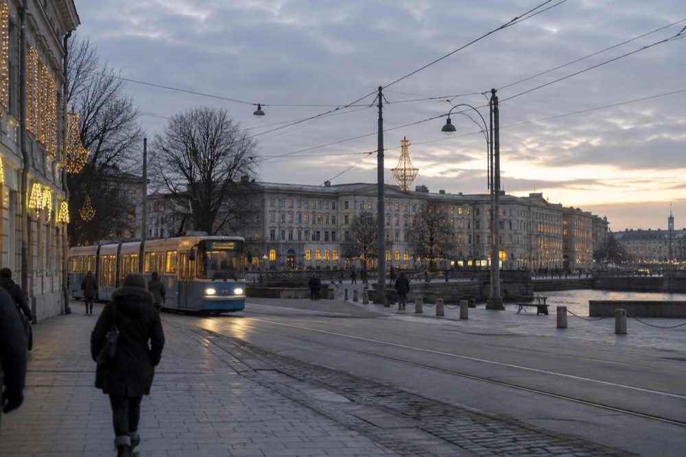A tram moving through a decorated city street with Christmas lights at dusk