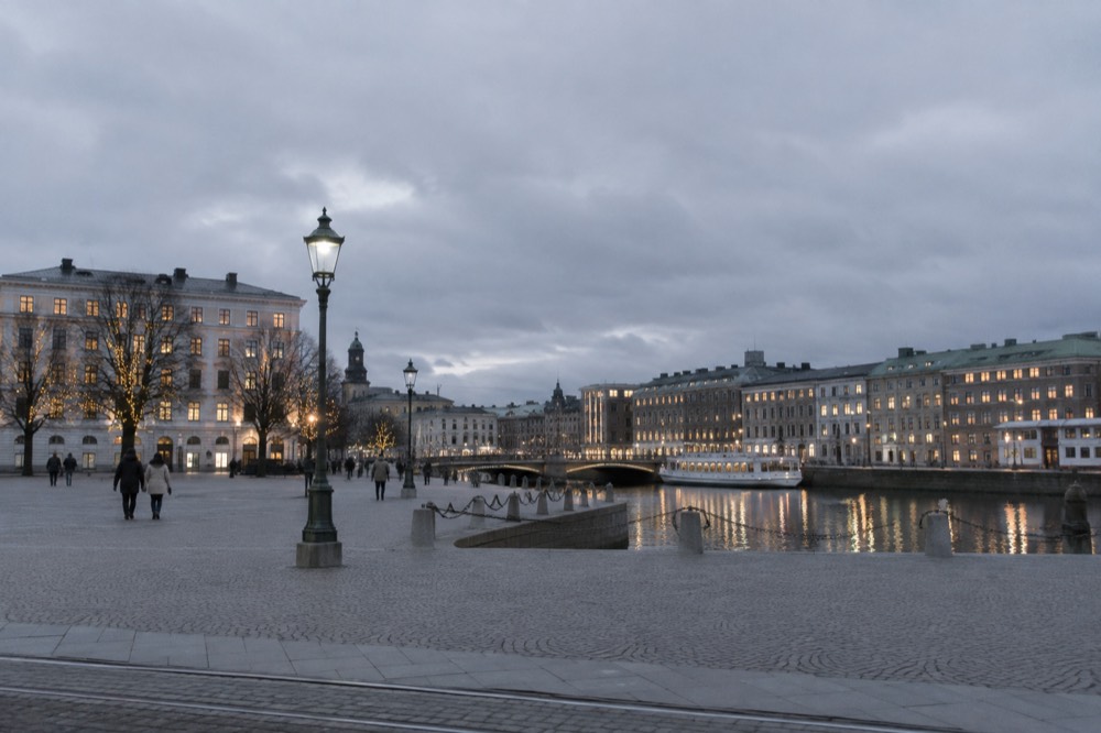 A city skyline with lit windows and festive illuminations reflected in a winter harbour