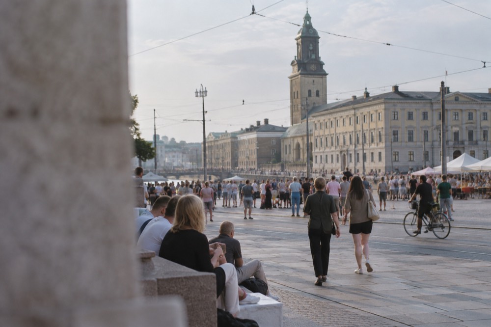 Crowds gathered in a sunlit Gothenburg square during a summer festival with the city hall and tram wires above