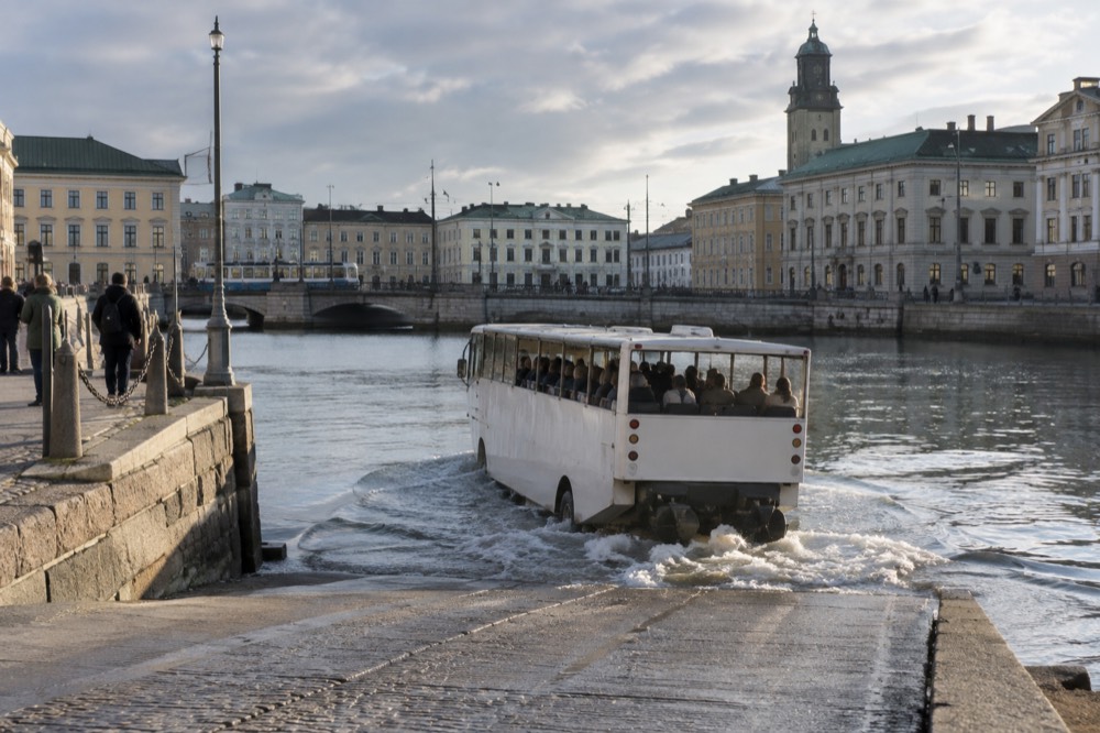 An amphibious sightseeing vehicle driving down a harbour ramp into the water with passengers aboard