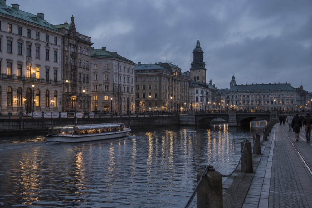 Gothenburg canal with sightseeing boat and old stone buildings under a grey sky
