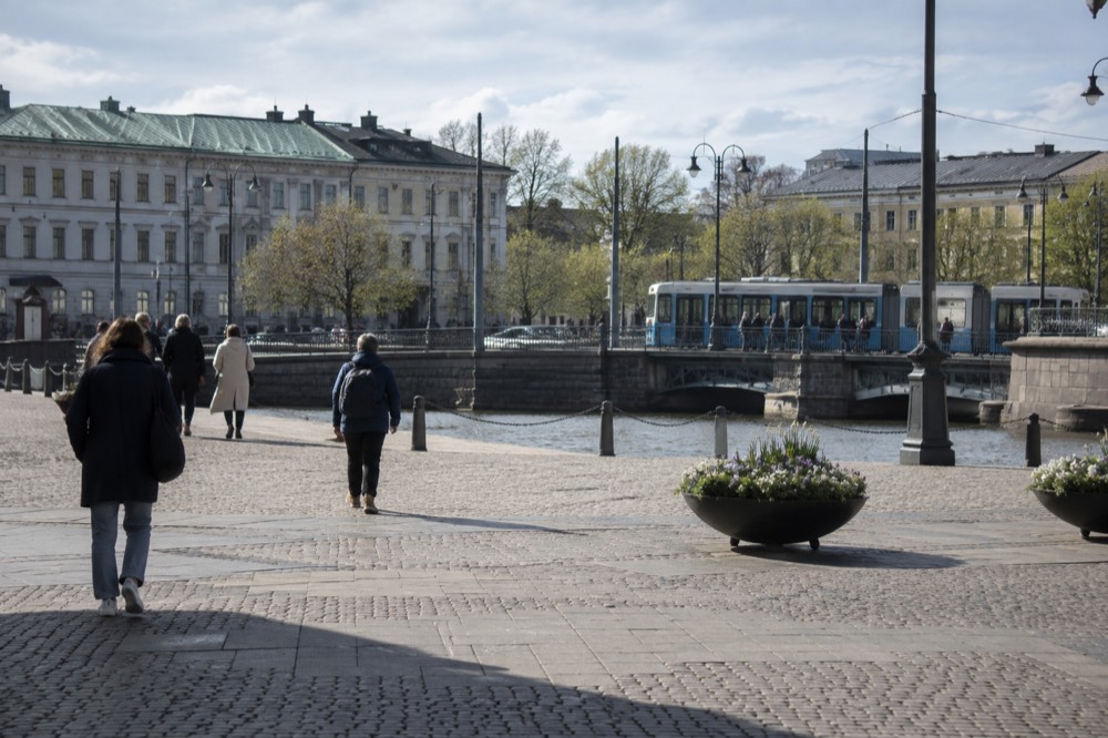 A blue Gothenburg tram at a stop with spring trees behind it