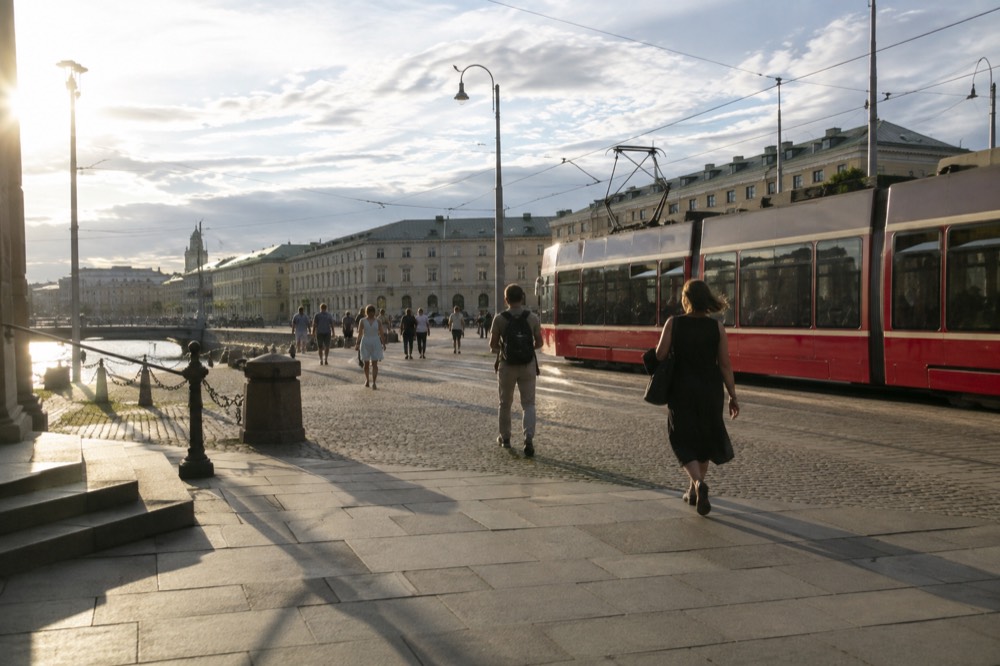 Red tram running along a Gothenburg street in bright summer light with people walking beside it
