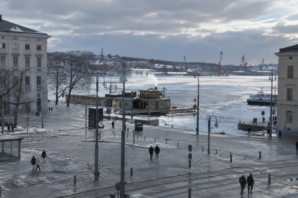 A steaming sauna by the water with a frozen archipelago harbour behind it