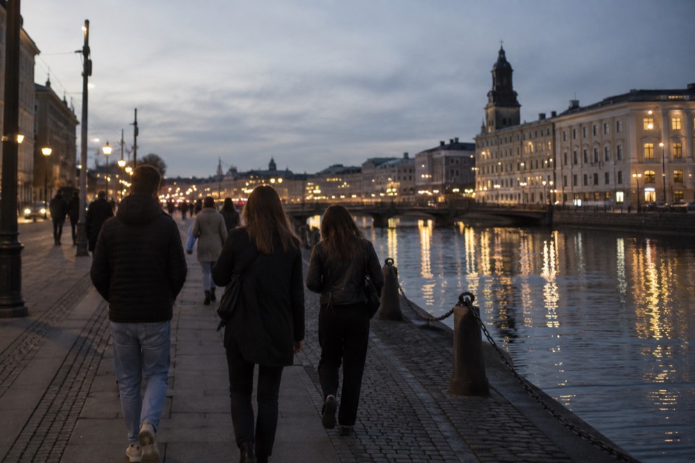Friends walking along a Gothenburg canal path at night with city lights reflected in the water