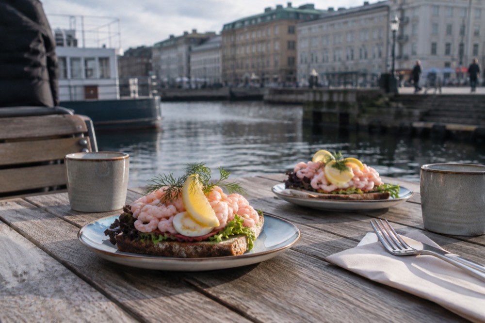 Open shrimp sandwiches on a wooden table beside a harbour in Gothenburg