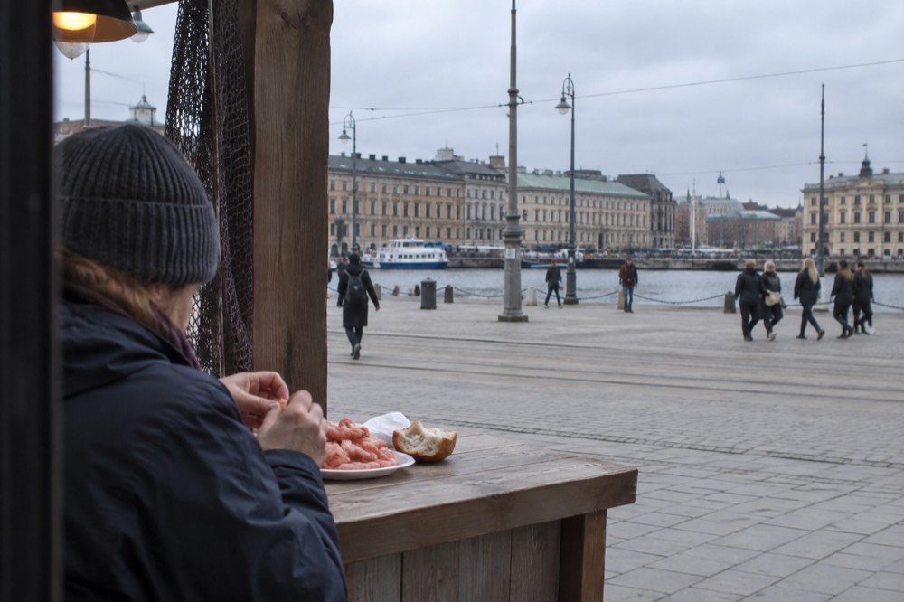 A person eating shrimp and bread at a wooden counter in a food hall