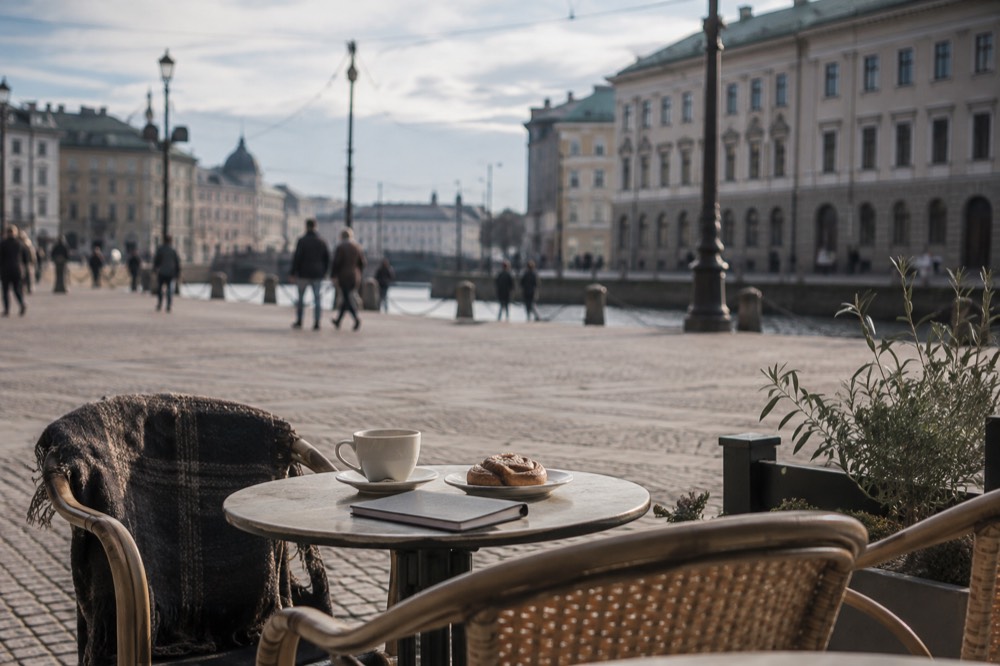 A coffee cup and cinnamon bun on a cafe table beside a notebook