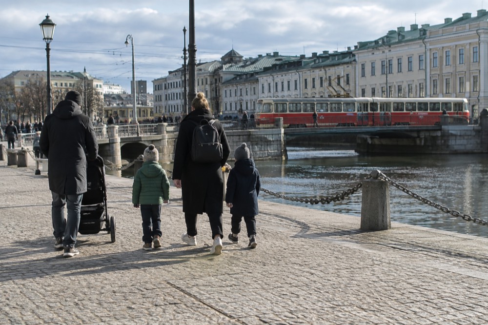 Families walking a granite quay in Gothenburg with a red tram passing behind them