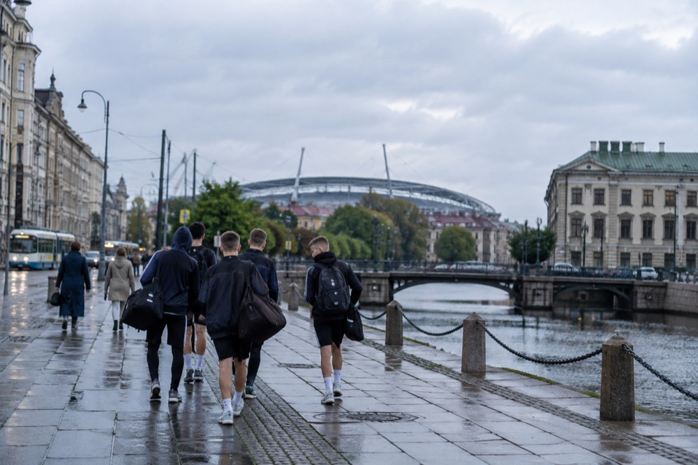 Youth football players walking along a Gothenburg avenue with the Ullevi stadium roofline behind them