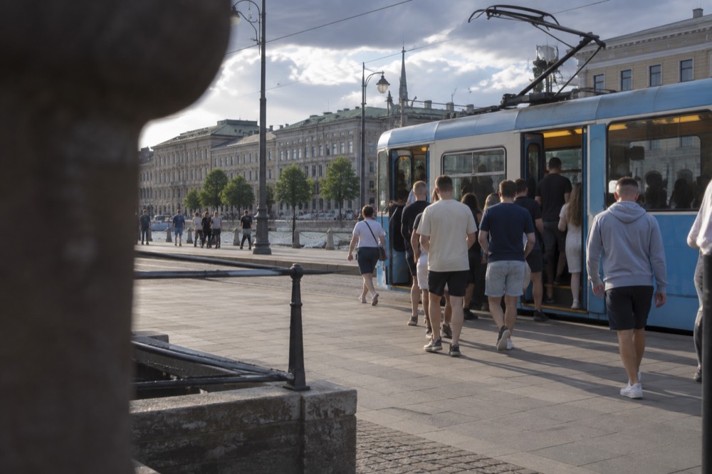 A blue Gothenburg tram at a stop with football supporters boarding on a summer evening