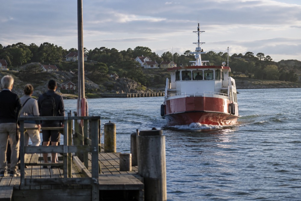 A red archipelago ferry approaching a wooden jetty on a car-free Gothenburg island in summer