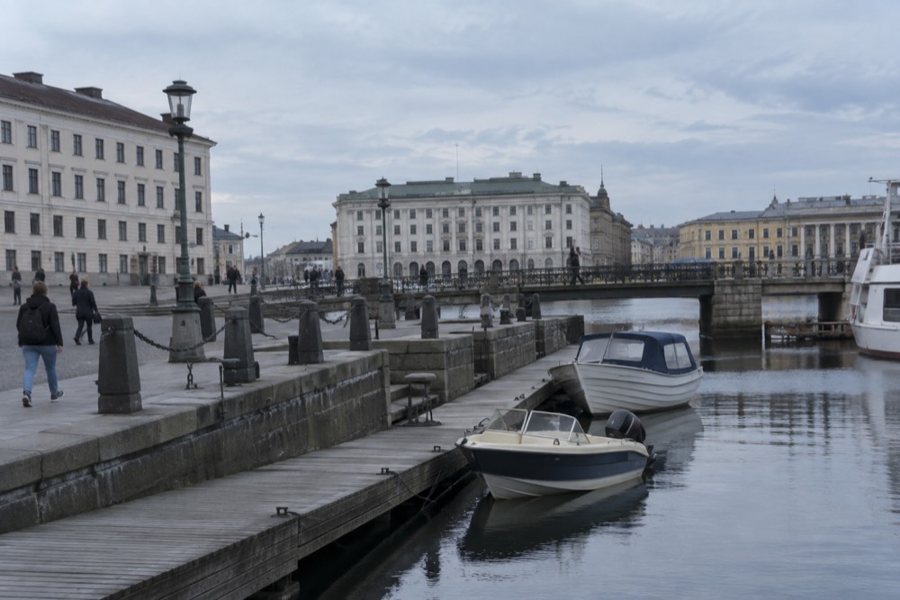 A quiet wooden walkway along a granite shoreline with small boats moored nearby