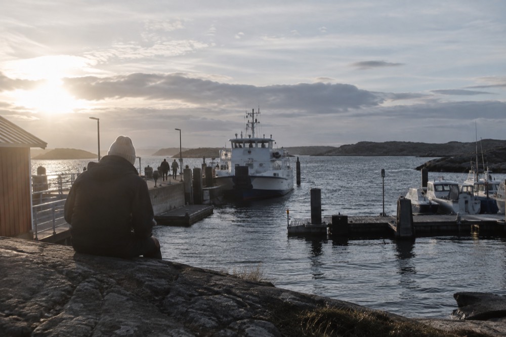 A passenger reading a ferry timetable board at the Saltholmen jetty in morning light