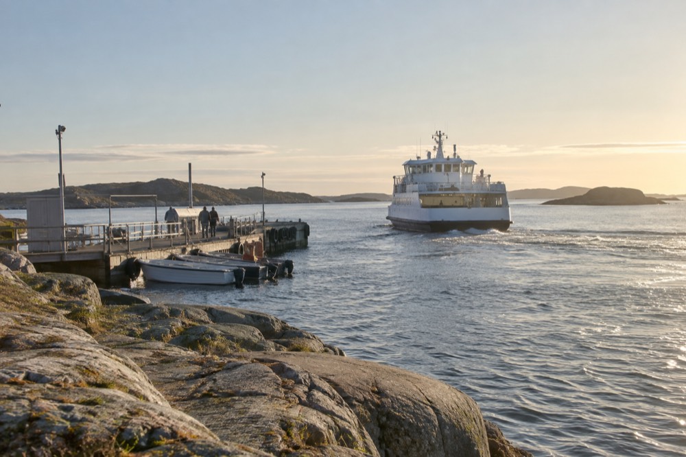A ferry pulling away from a rocky island jetty at golden hour in the Gothenburg archipelago