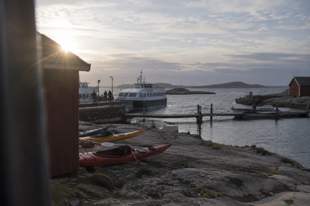 Kayaks resting on a smooth granite shoreline with red wooden boathouses and open sea beyond