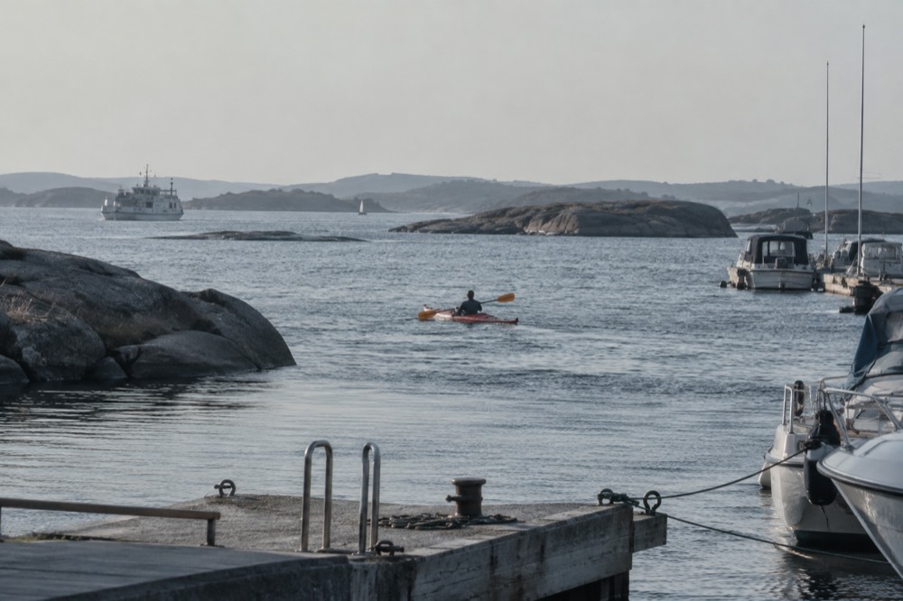 A kayak paddler crossing open water between low granite skerries in soft evening light