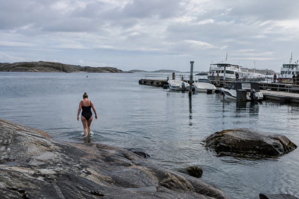 A swimmer stepping into calm blue sea from a flat rock with skerries behind
