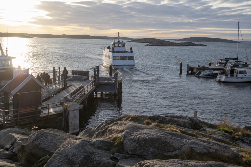 A wooden island jetty with a ferry pulling away and granite rocks in the foreground