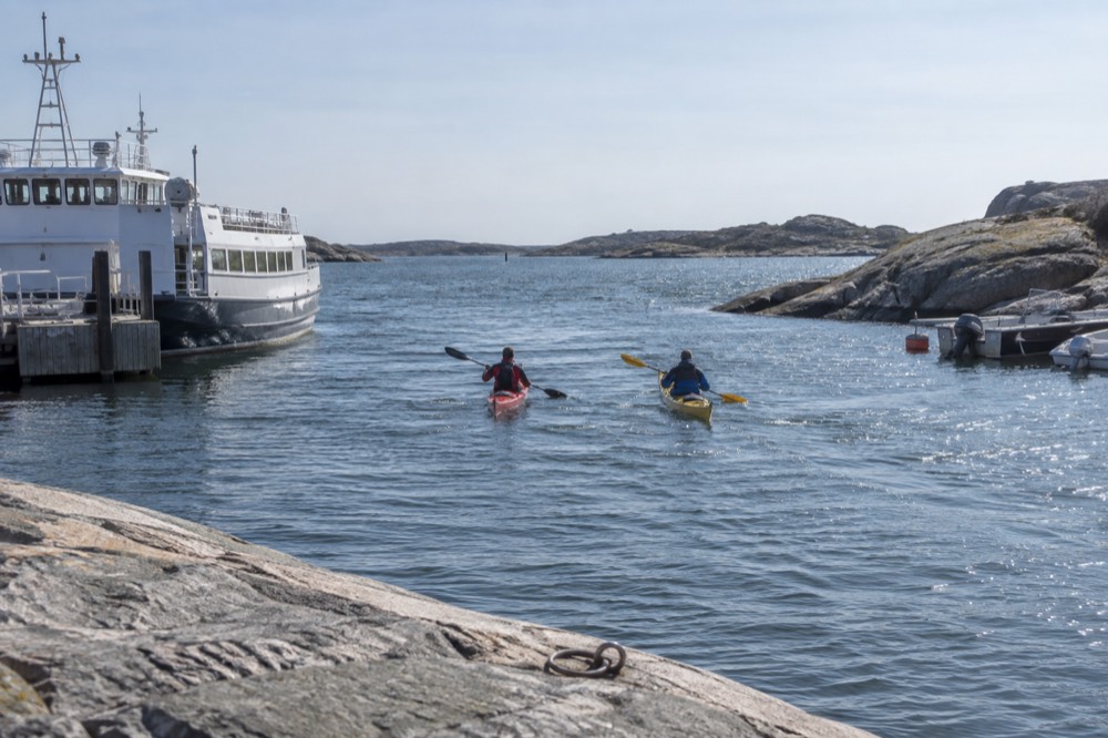 Two kayaks paddling side by side through a narrow sheltered channel between rocky islands