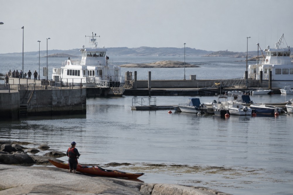 A paddler in a buoyancy aid checking a map on a kayak deck beside rocky shore