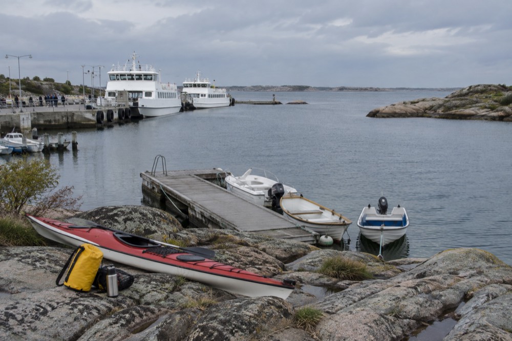 A dry bag and thermos packed on rocks beside a kayak at a small island jetty