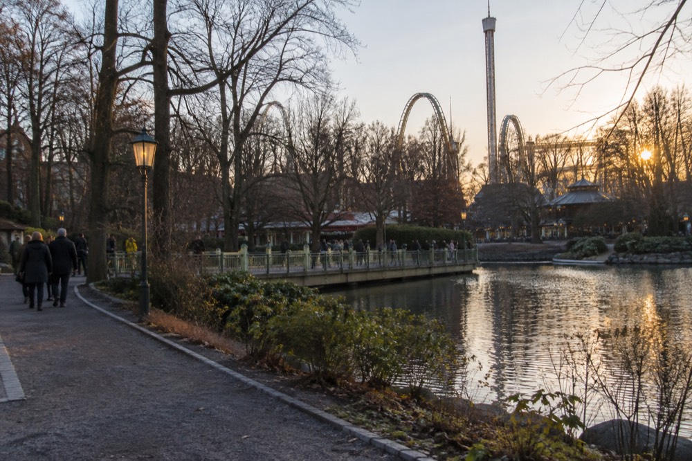 Park guests on a bridge with rides in the background at golden hour