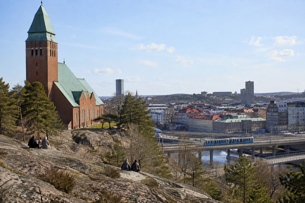 A blue Gothenburg tram crossing a bridge with the city skyline behind it