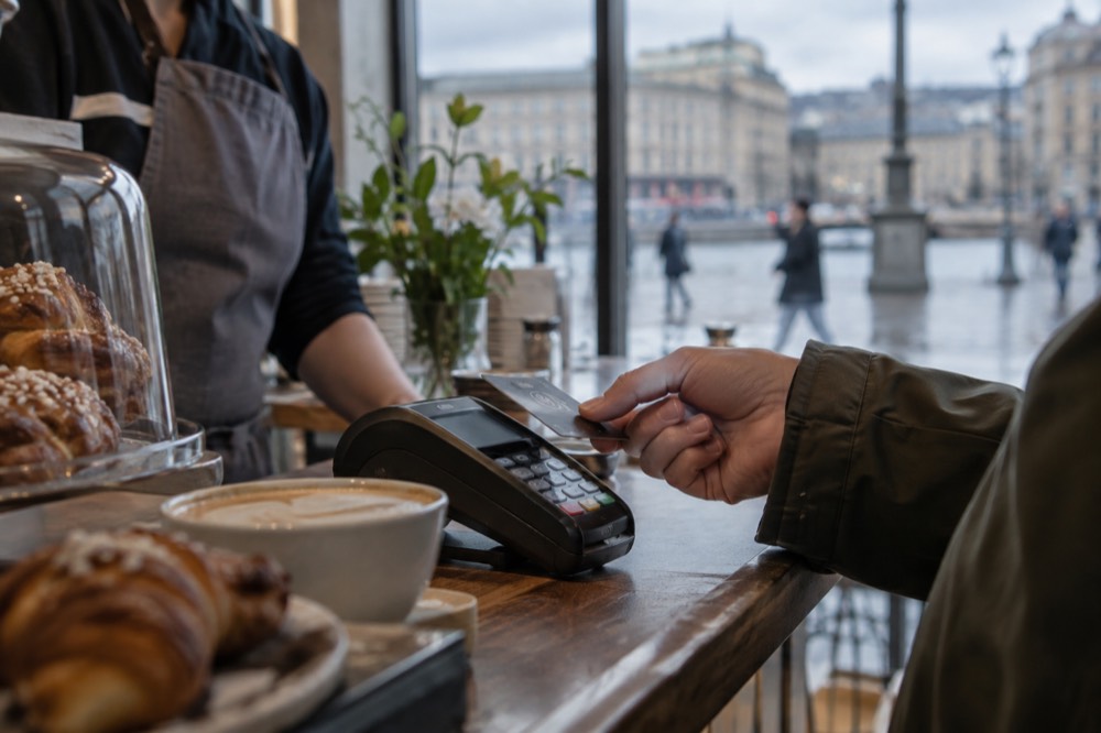 A contactless card being tapped on a payment terminal at a Gothenburg cafe counter