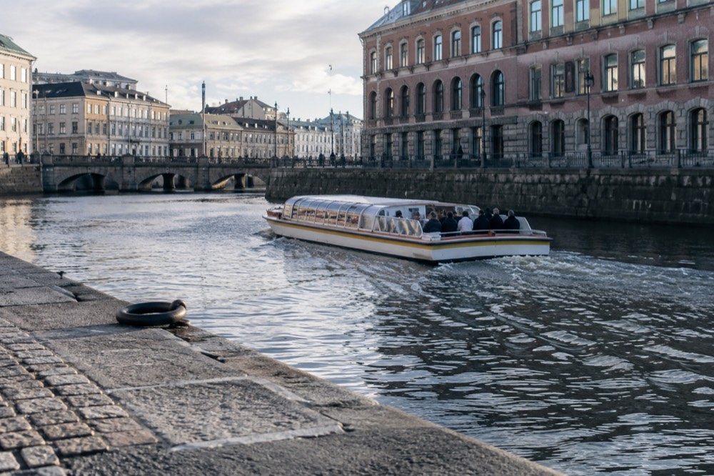 A low open tour boat gliding along a city canal beside red brick buildings in Gothenburg