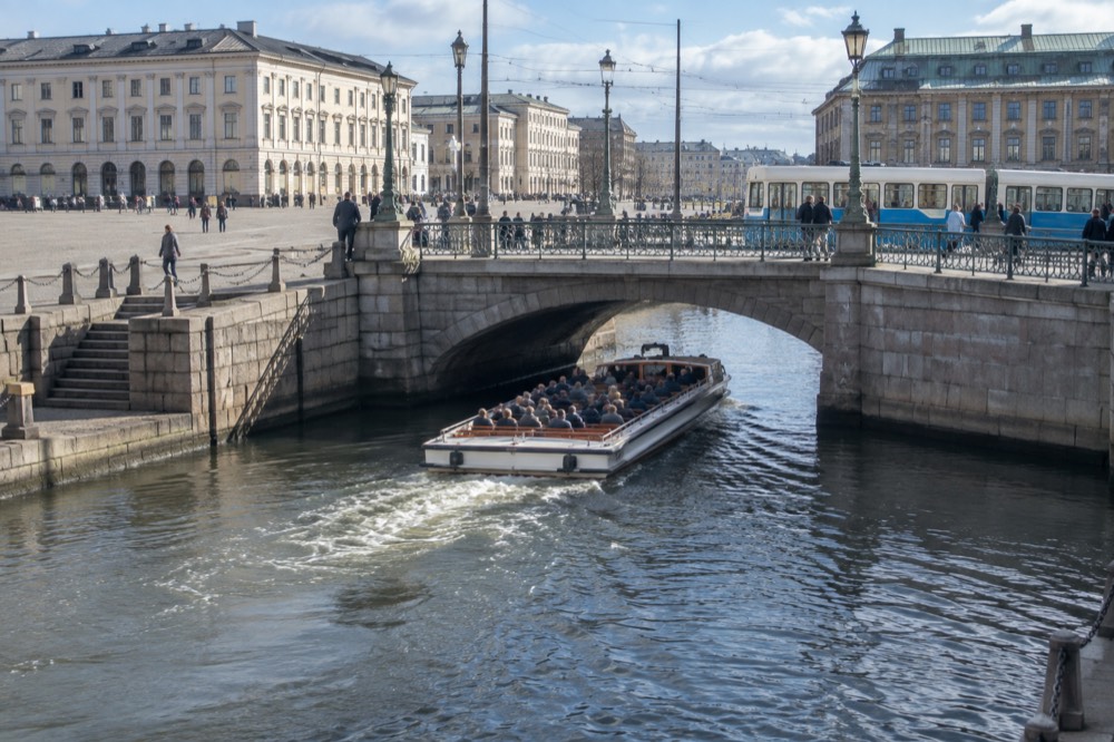Tour boat passengers passing under a low stone bridge in a Gothenburg canal