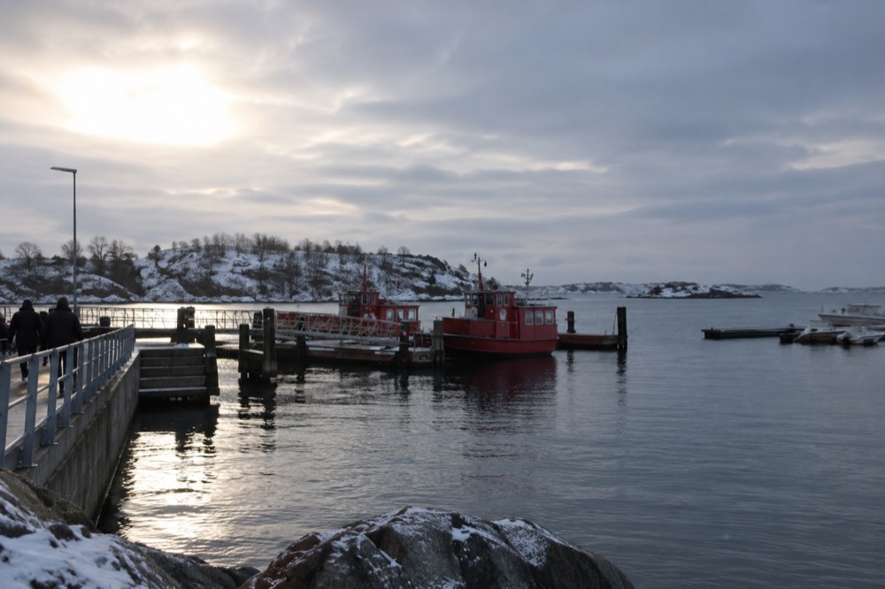 Red ferry boats moored at a small wooden jetty on a snow-dusted island in winter light