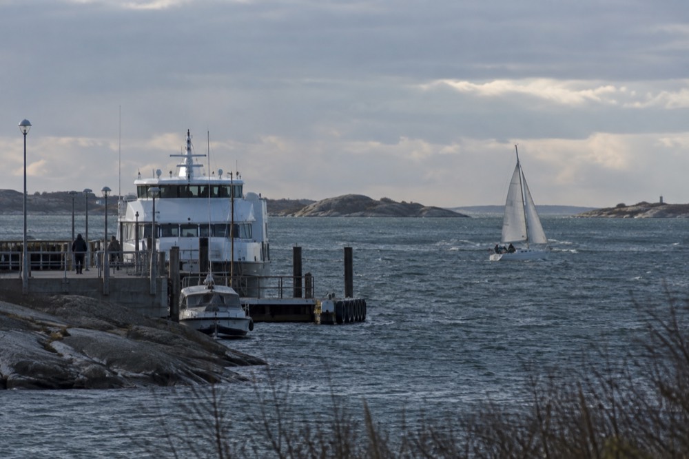 A small sailing boat heeling slightly on dark winter water with low islands behind