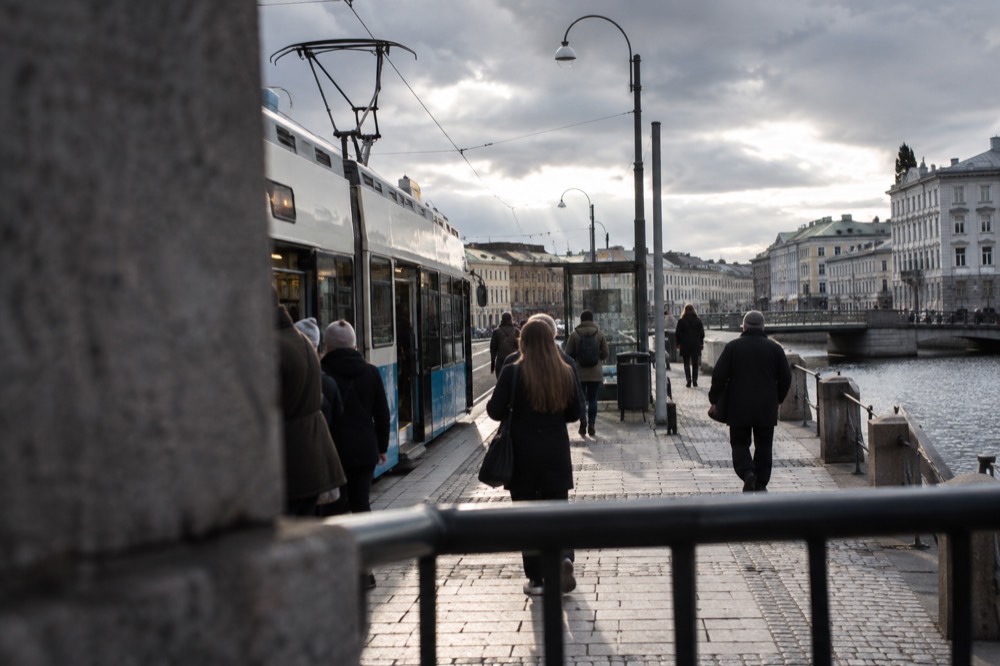 A Gothenburg tram at a stop with passengers boarding near the canal