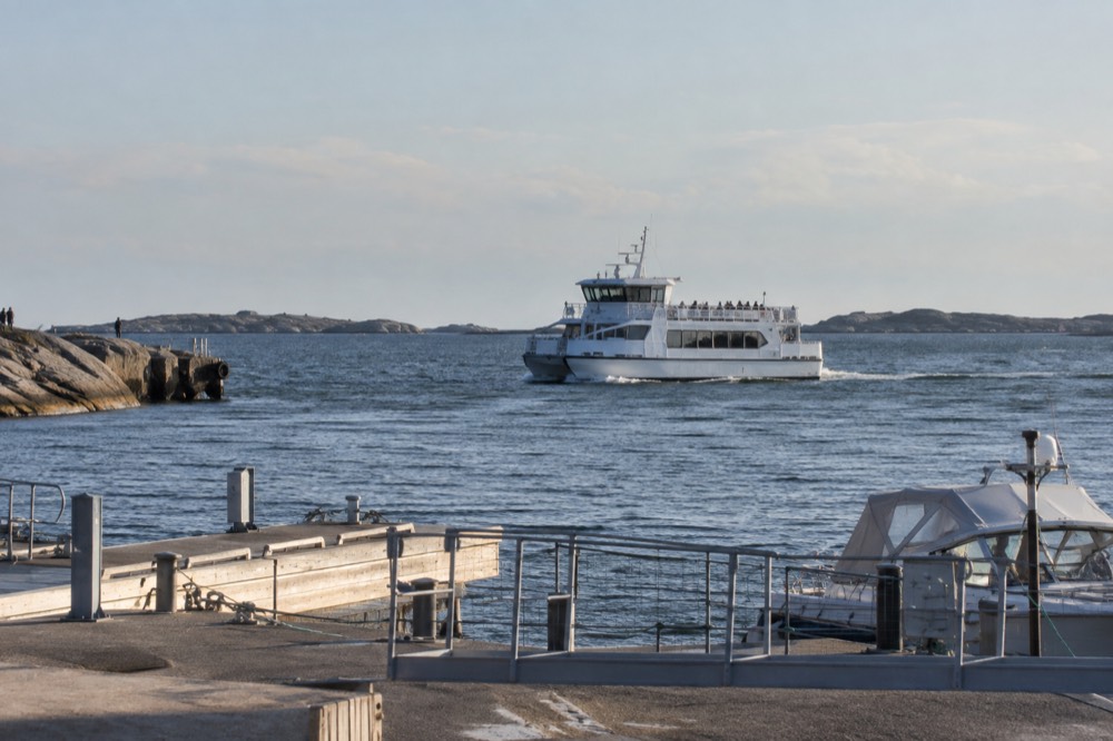 A white passenger ferry crossing open water between low granite islands on a bright day
