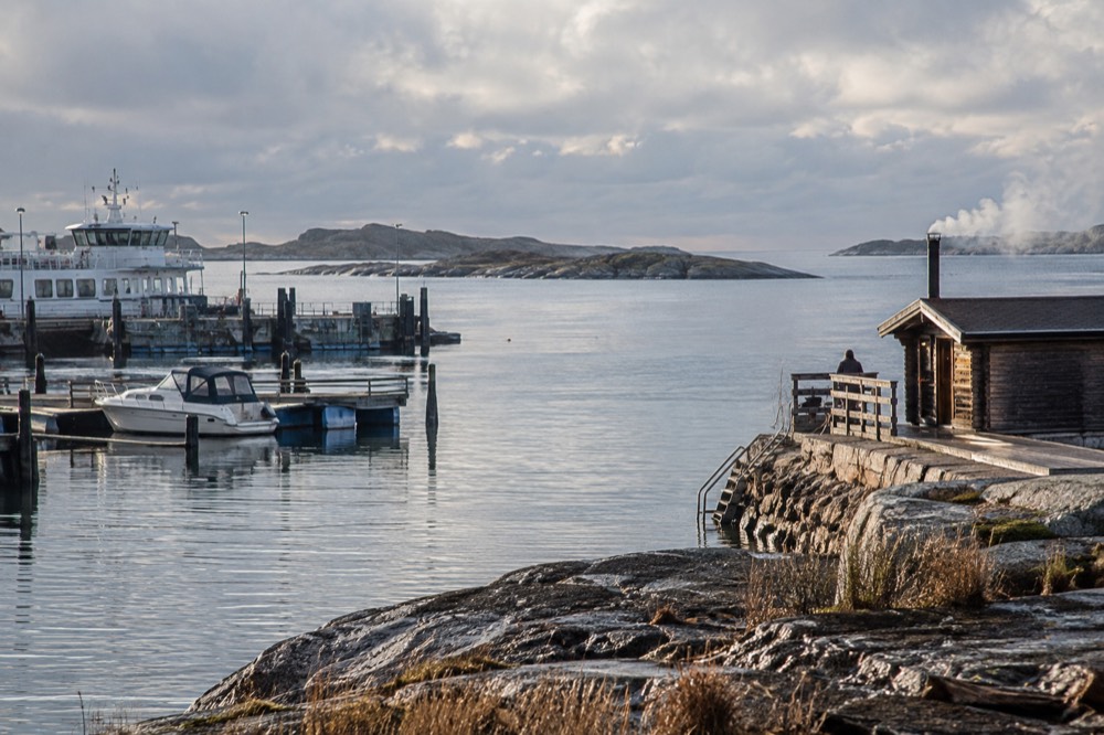 A wood-fired sauna at the end of a rocky jetty with steam rising over still water