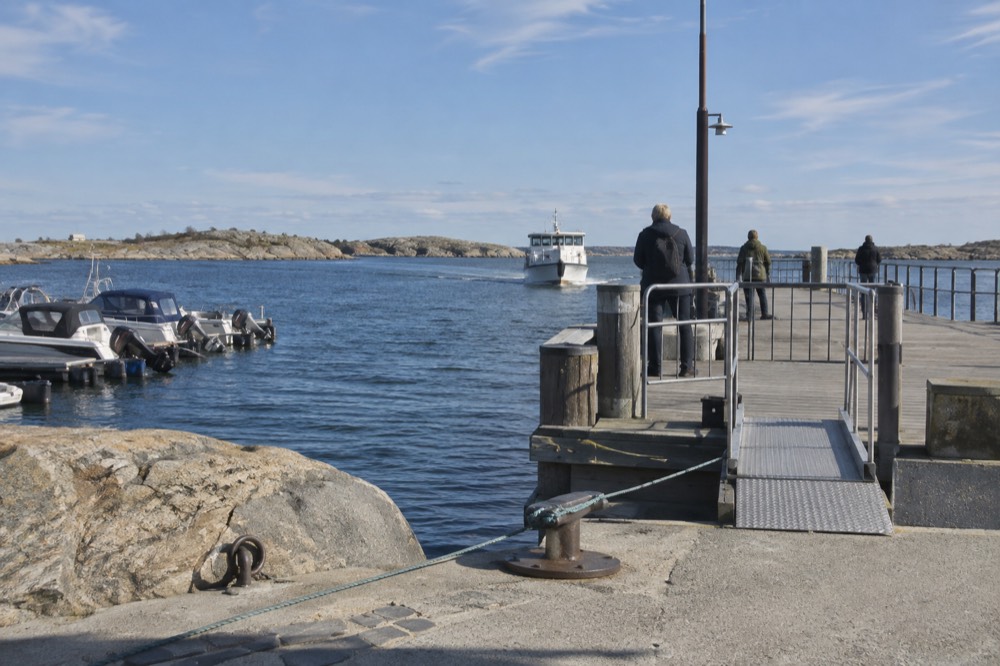 A wooden ferry pier with a small white boat approaching across blue water