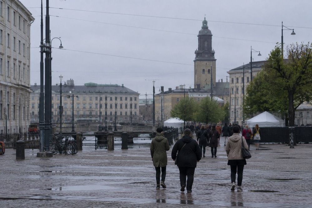 Festivalgoers in light rain jackets walking a tree-lined path between stages