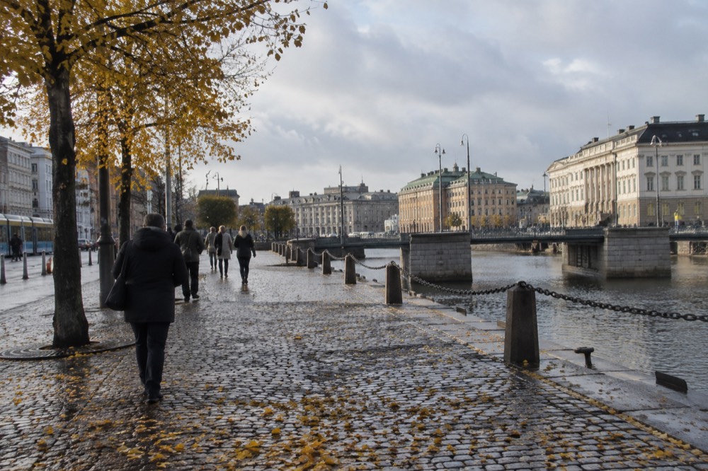 Wet cobblestone street in Gothenburg with autumn leaves and people in rain jackets