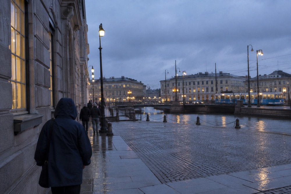 Rain jacket hood up on a person walking past a granite building in Gothenburg