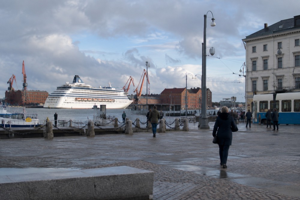 A large cruise ship tied up at a Scandinavian harbour quay with red brick warehouse buildings and harbour cranes behind it
