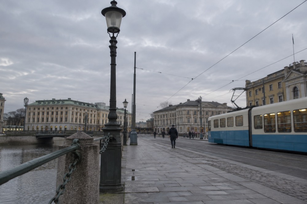 A Gothenburg tram in blue and cream livery crossing a stone-paved street near the canal