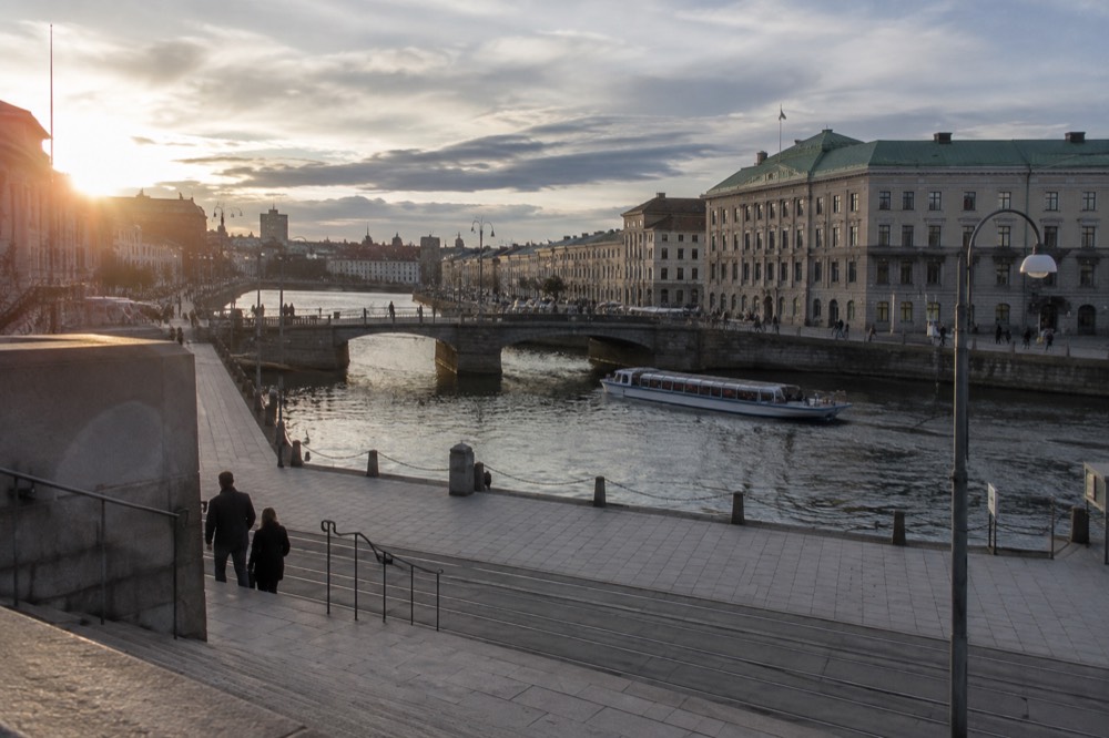 Gothenburg canal with a sightseeing boat passing under a stone bridge in evening light