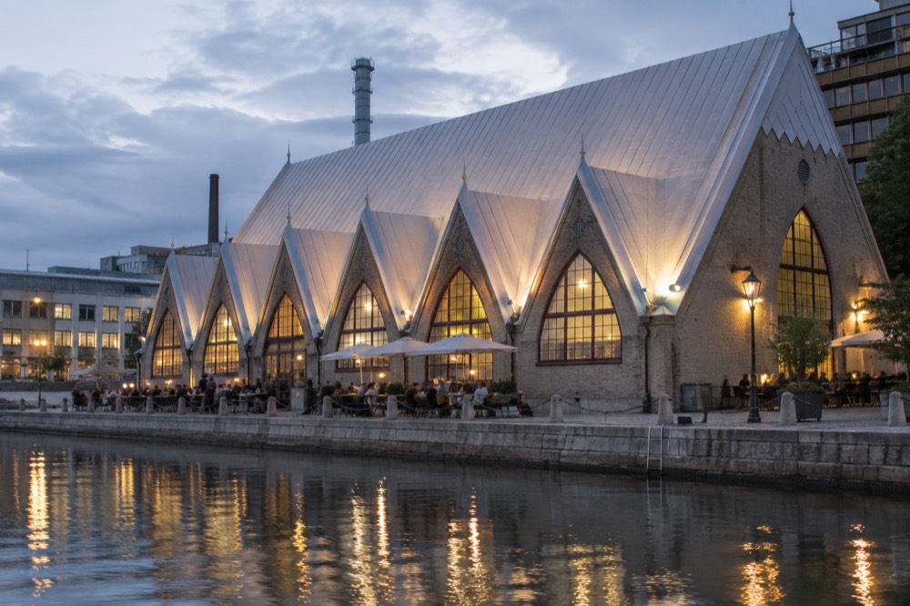 Feskekorka fish market hall lit up in the evening with people at outdoor tables