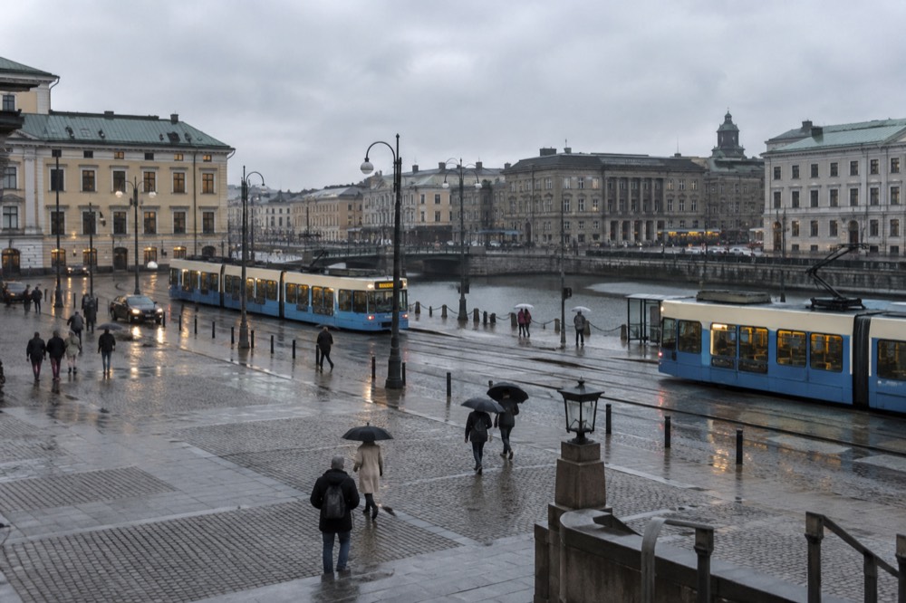 Wet cobblestone street in central Gothenburg with trams passing and people with umbrellas