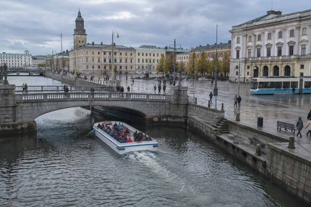 Open sightseeing boat passing under a low stone bridge on a Gothenburg canal
