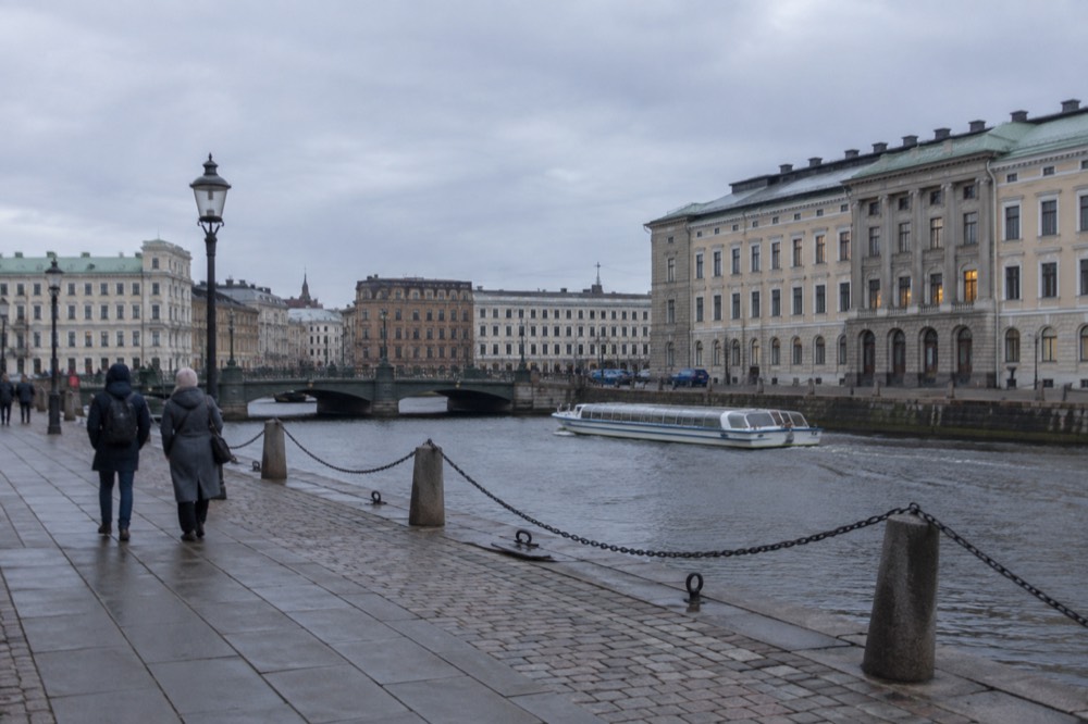Gothenburg canal with sightseeing boat and stone buildings under grey sky